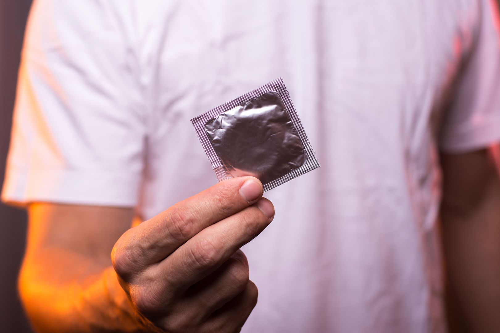 Unknown man in white shirt holding condom in hand, closeup. Safety sex concept. 