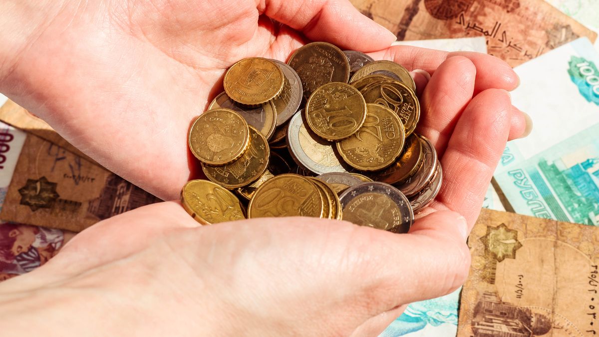 Female hands with money over banknote background. Euro coins Euro cents.