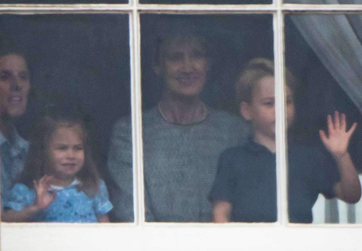 Księżniczka Charlotte i książę George stroją miny w oknie Pałacu Buckingham