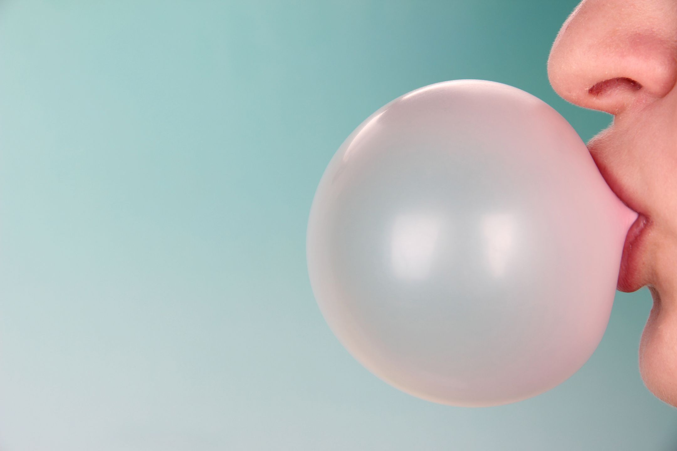 Person doing bubble with chewing gum on bright background