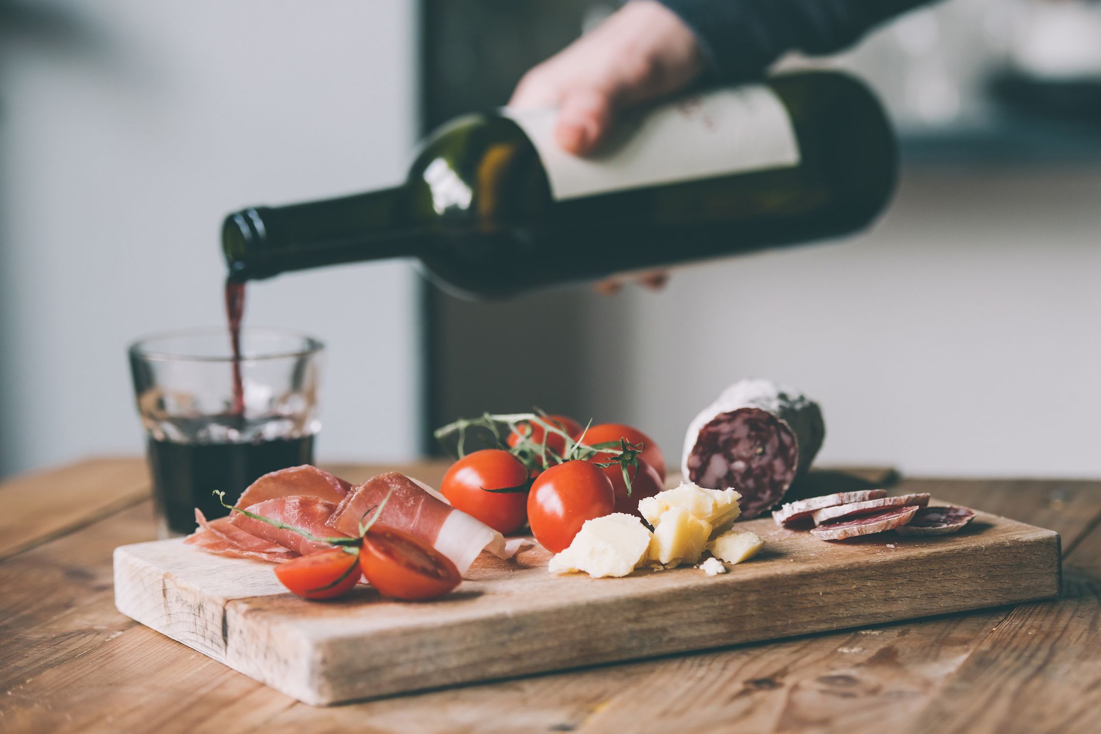 Appetizers - tomato, meat and cheese - on wooden board with bottle of wine and glass. Toned image