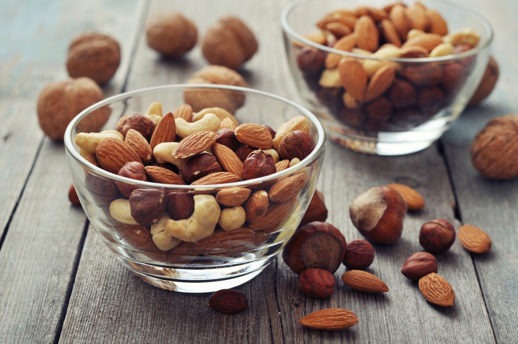 Almonds, walnuts, cashew and hazelnuts in glass bowls on wooden background
