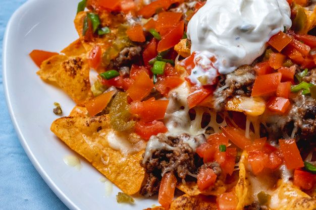 side view nachos tortilla chips with grilled ground meat tomato spring onion tomato cheese jalapeno pepper and sour cream on top