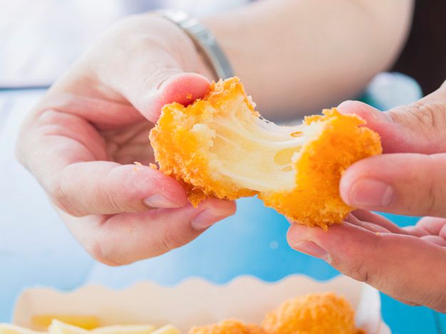 Hand is holding a stretch cheese ball ready to be eaten with soft focused french fries on blue table background