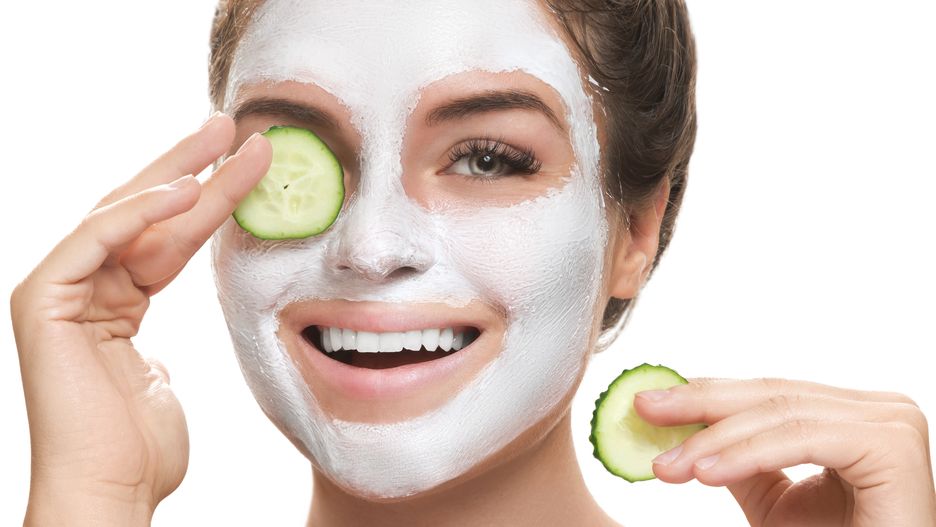 Woman with facial mask and cucumber slices in her hands on white background