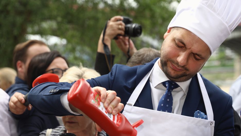 Patryk Jaki starannie polewa kiełbasę keczupem