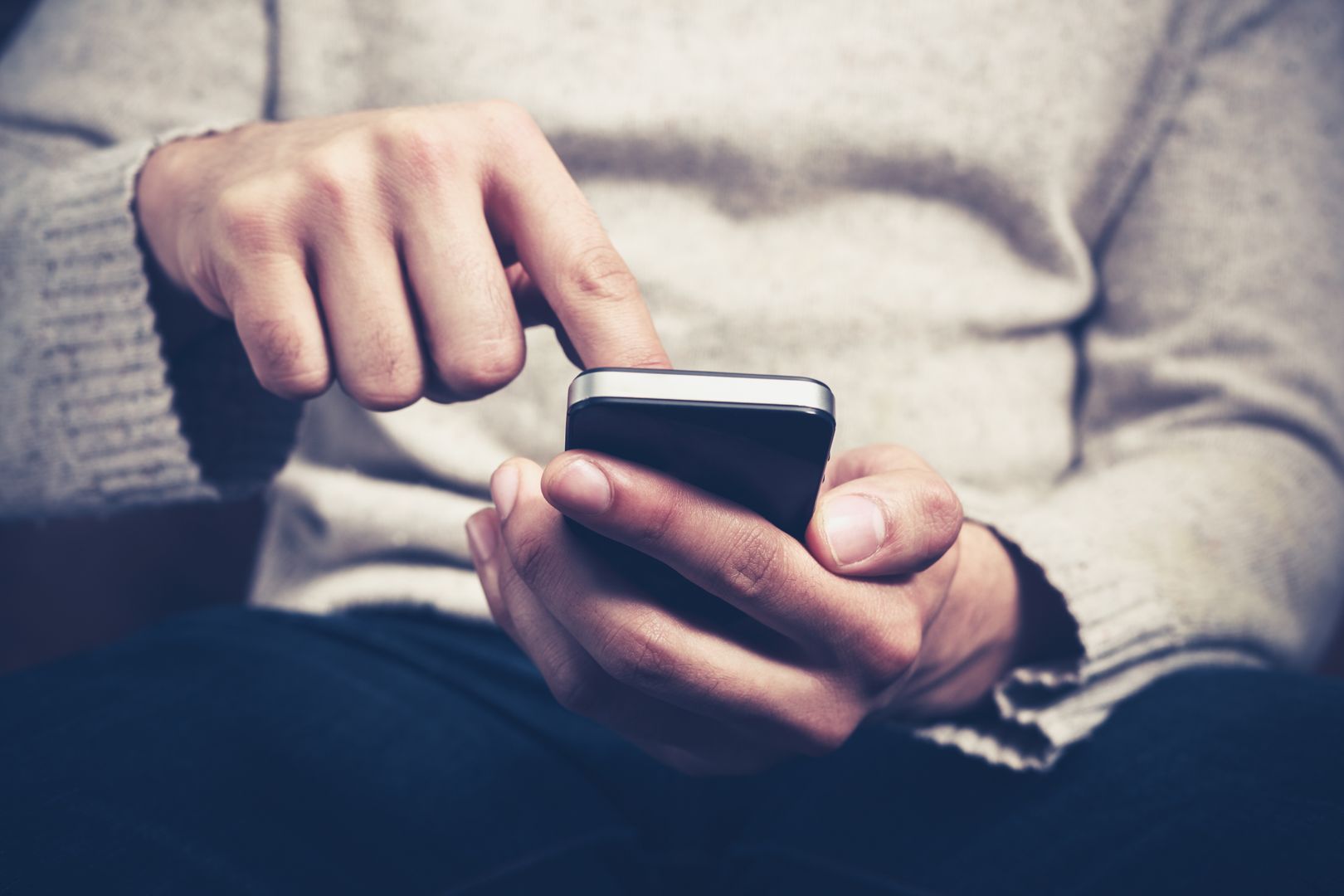 Closeup on a man's hands as he is sitting on a sofa and using a smartphone