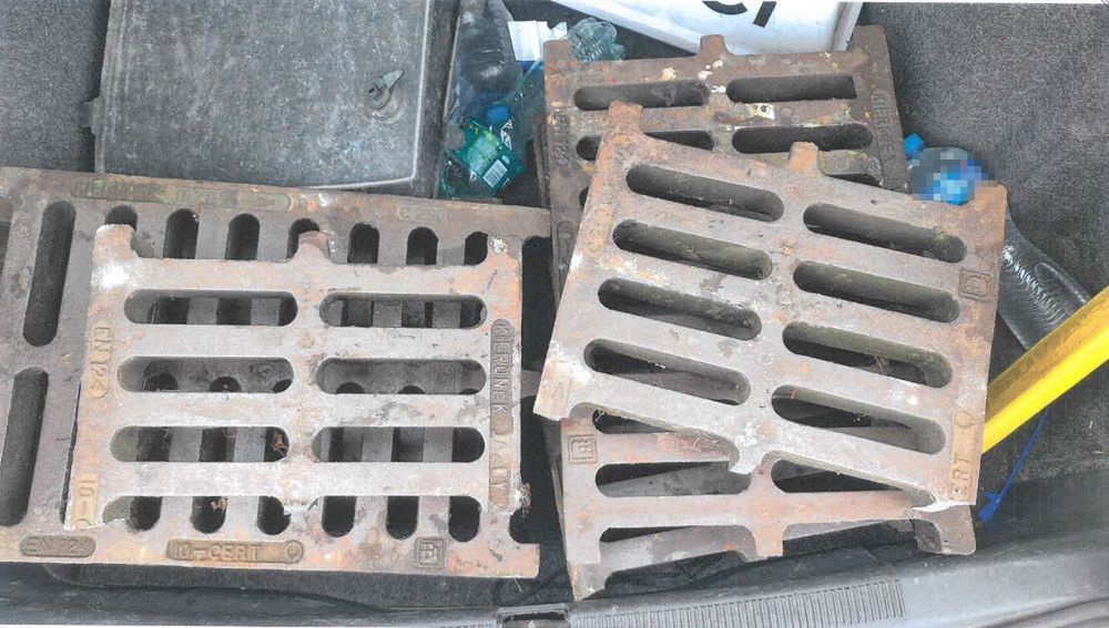 W bagażniku samochodu znajdują się metalowe kratki, obok nich leżą plastikowe butelki i narzędzia.