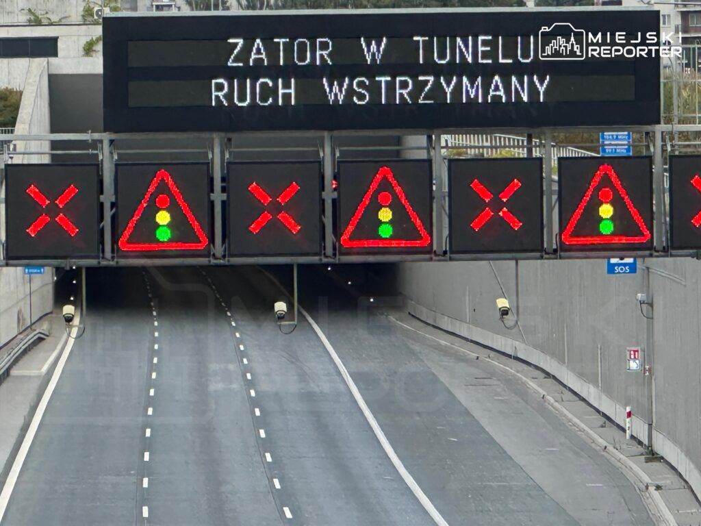 Na elektronicznym panelu informacyjnym widoczne są czerwone znaki „X” oraz zielone światło, informujące o zatorze w tunelu.