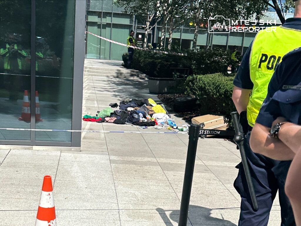 Policjant w kamizelce odblaskowej obserwuje miejsce zdarzenia, gdzie leżą porozrzucane ubrania na chodniku.