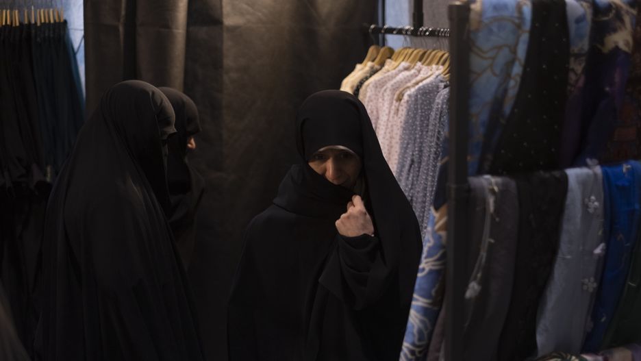 Veiled women are standing together next to dresses while shopping at the Hijab and Chastity fair in the Imam Khomeini Grand Mosque in downtown Tehran, Iran, on March 28, 2024. Amir Hossein Bankipour, a Member of the Iranian Parliament from Isfahan and a member of the Cultural Commission, is saying on the ''Ofogh TV program'' that after the Nowruz (Iranian New Year) holidays, if a woman does not wear a hijab, she will not be fined by the police, but 30,000,000 Rials (49 USD) will be automatically deducted from her personal bank account. (Photo by Morteza Nikoubazl/NurPhoto via Getty Images)