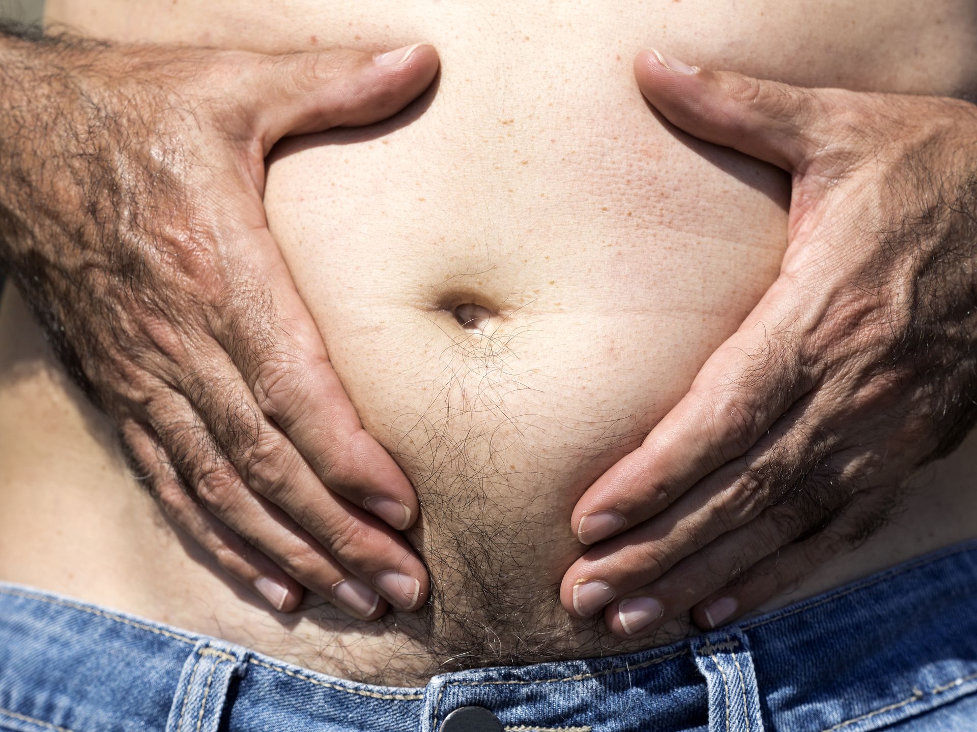 A close-up image of a men mature with  belly fat pinching itself, white-skinned, with jeans shorts in the light of the Sun in the beach
Belly of a man with some belly fat. Abdominal fat. Valencia, Spain.
Jose A. Bernat Bacete