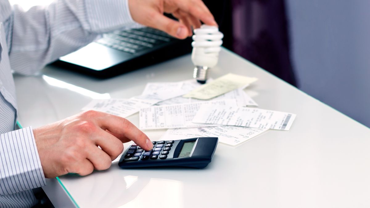 Na zdjęciu mężczyzna liczący, ile zaplaci za prąd. Na biurki rachunki oraz kalkulator