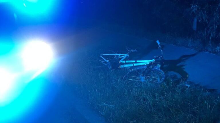 Rower leżący na poboczu drogi, oświetlony niebieskimi światłami policyjnymi w nocy.