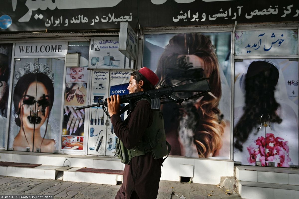 Talibski bojownik przechodzi obok salonu piękności ze zniszczonymi plakatami 