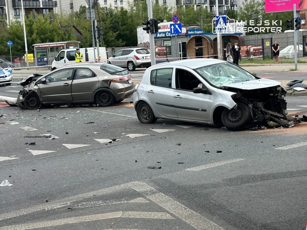 Dwa uszkodzone samochody osobowe na skrzyżowaniu, z rozrzuconymi fragmentami karoserii na jezdni.