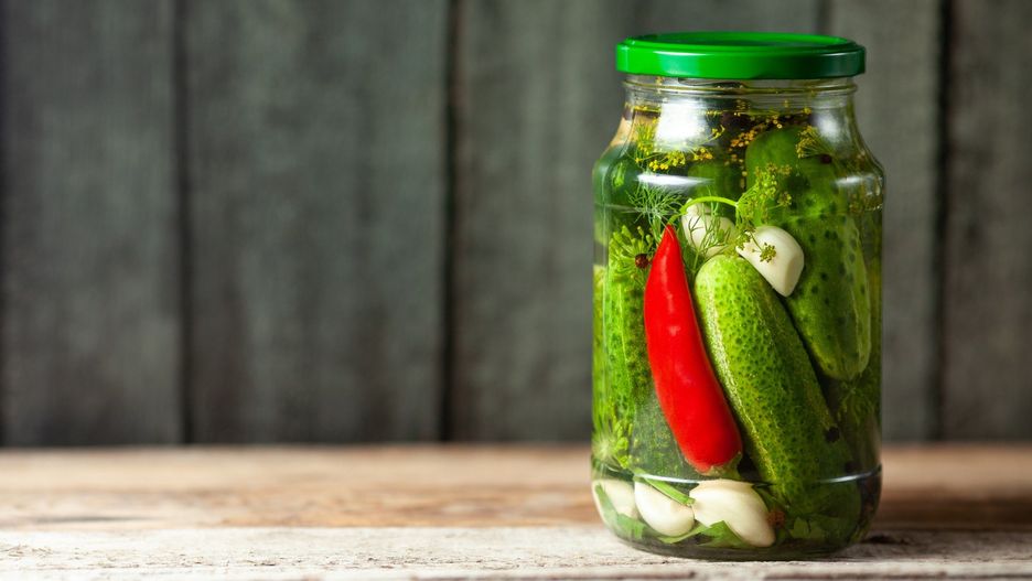 Pickled cucumbers in glass jars on wooden background