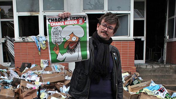 Dziennikarz "Charlie Hebdo" z poprzednią kontrowersyjną okładką gazety stoi przed zdewastowaną siedzibą redakcji