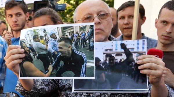 Mężczyzna pokazuje zdjęcia z demonstracji, na której pobito dziennikarzy