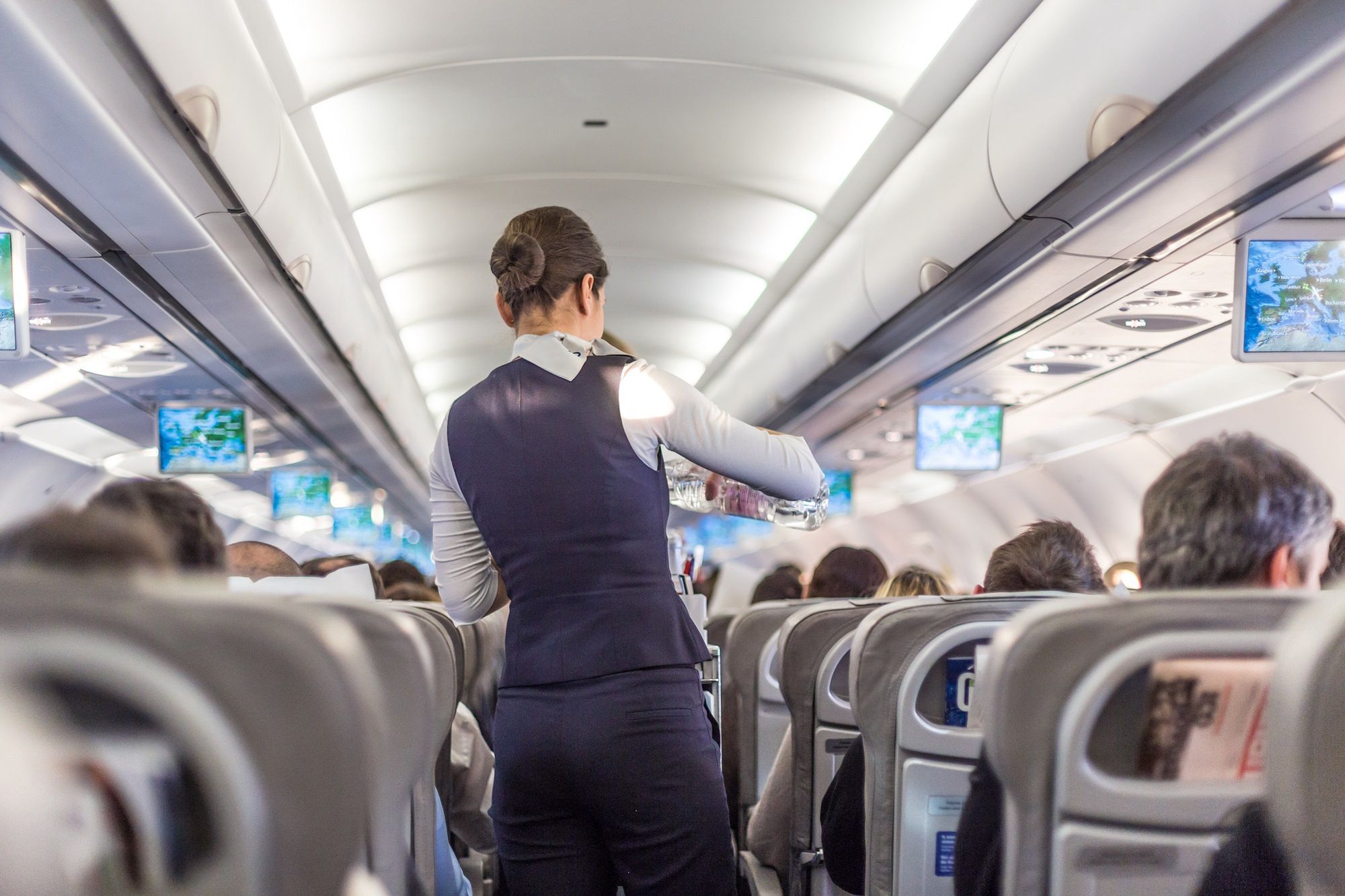 Interior of commercial airplane with stewardess serving passengers on seats during flight.Interior of commercial airplane with flight attandant serving passengers on seats during flight. Stewardess in dark blue uniform walking the aisle. Horizontal composition.stewardess, flight attandant, airplane, aeroplane, aircraft, interior, air, plane, cabin, crowded, flight, transport, transporation, passengers, people, airline, aisle, job, business, carrier, chairs, commercial, corridor, economy, entertaiment, passenger, indoor, inside, jet, journey, light, man, modern, multimedia, public, row, screen, seat, seating, service, sky, tourism, tourist, transportation, travel, trip, voyage, work, serve, rear, stewardess, flight attandant, airplane, aeroplane, aircraft, interior, air, plane, cabin, crowded, flight, transport, transporation, passengers, people, airline, aisle, job, business, carrier, chairs, commercial, corridor, economy, entertaiment, passenger, indoor, inside, jet, journey, light, man, modern, multimedia, public, row, screen, seat, seating, service, sky, tourism, tourist, transportation, travel, trip, voyage, work, serve, rear