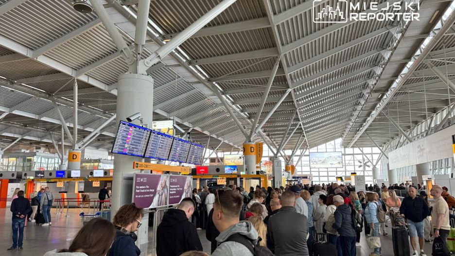 Tłum ludzi czekający w kolejce przy stanowiskach odprawy na nowoczesnym lotnisku.