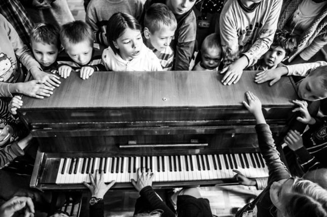 Pierwsze z wyróżnionych zdjęć przedstawia niesłyszące dzieci zebrane wokół pianina. Obraz ten stanowi zdjęcie otwarcia dla cyklu Marka pod tytułem „Pięć zmysłów”, w którym opowiada o życiu i postrzeganiu świata przez osoby z niepełnosprawnościami, w tym przypadku jest to upośledzenie zmysłu słuchu. Fotografia powstała podczas zajęć muzycznych dla niesłyszących dzieci, które poprze dotyk mogły czuć muzykę. To emocjonalne zdjęcie świetnie podkreśla jak w przypadku wykreślenia jednego ze zmysłów inne, jak np. dotyk, rozkwitają.