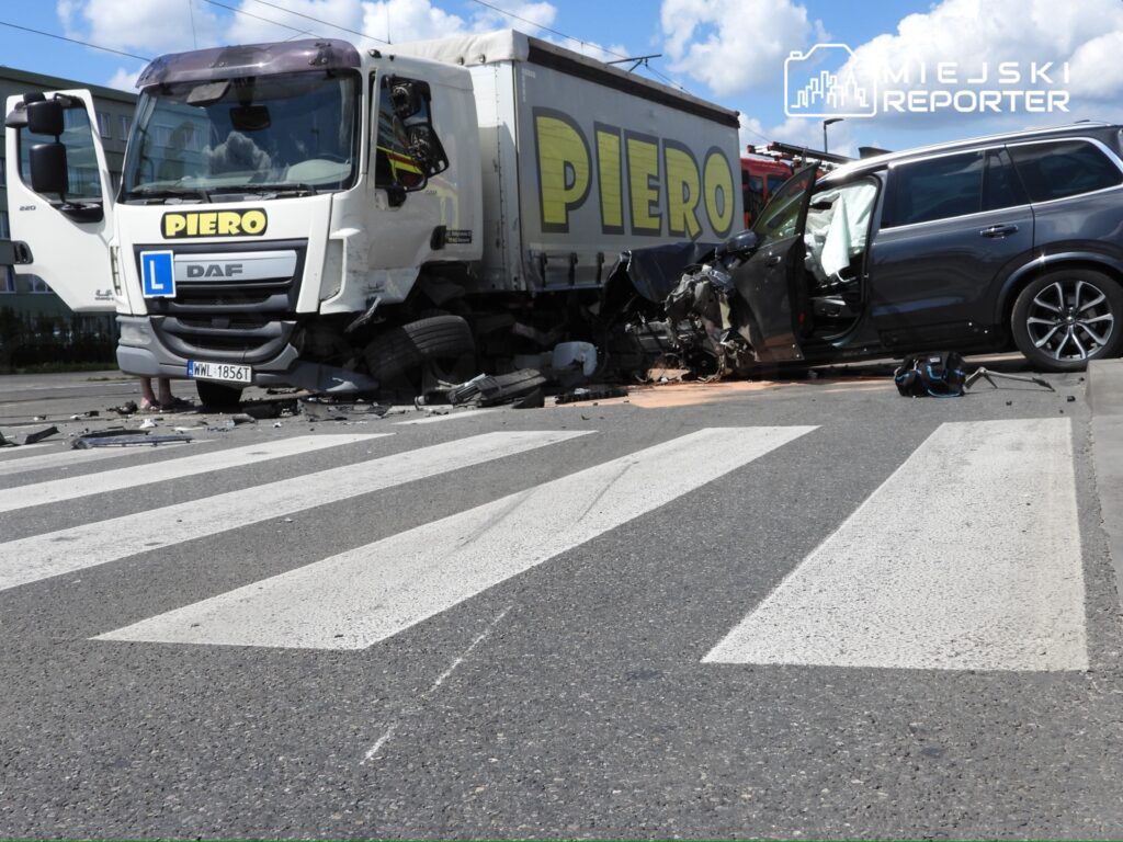 Zderzenie ciężarówki z osobowym samochodem na przejściu dla pieszych, uszkodzone pojazdy na drodze.