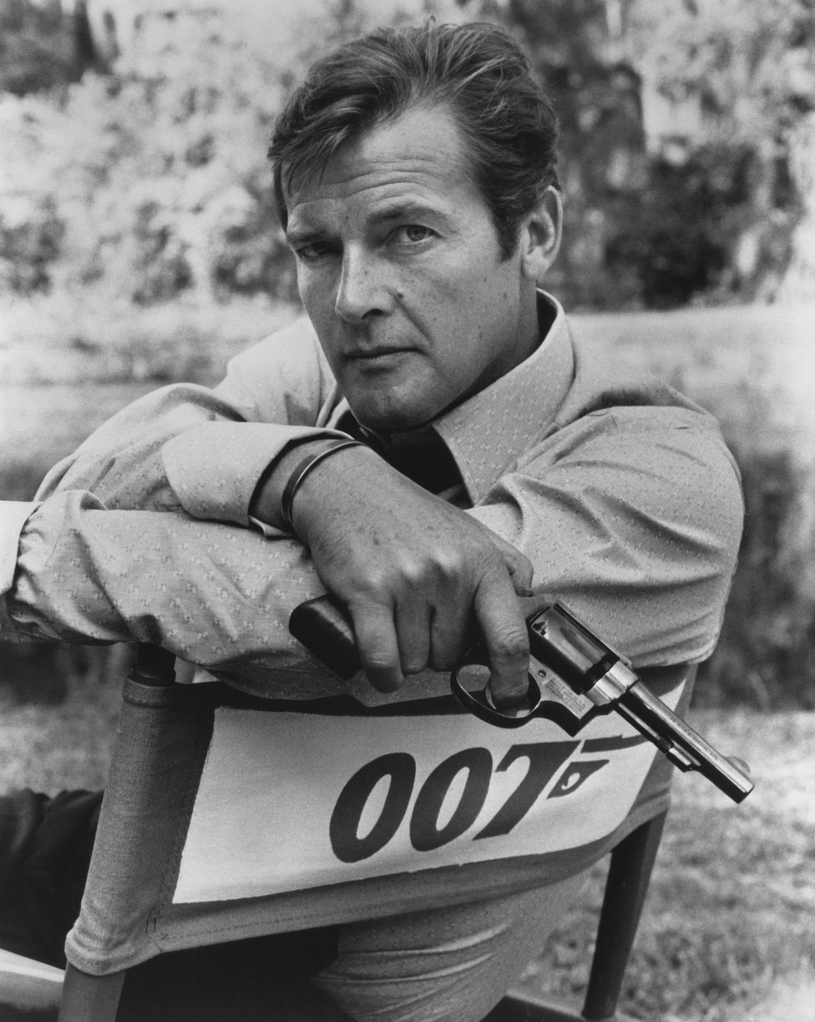 Roger Moore poses in director's chair with 007 logo holding gun as James Bond in a publicity portrait for the 1973 film 'Live and Let Die'. (Photo by Screen Archives/Getty Images)