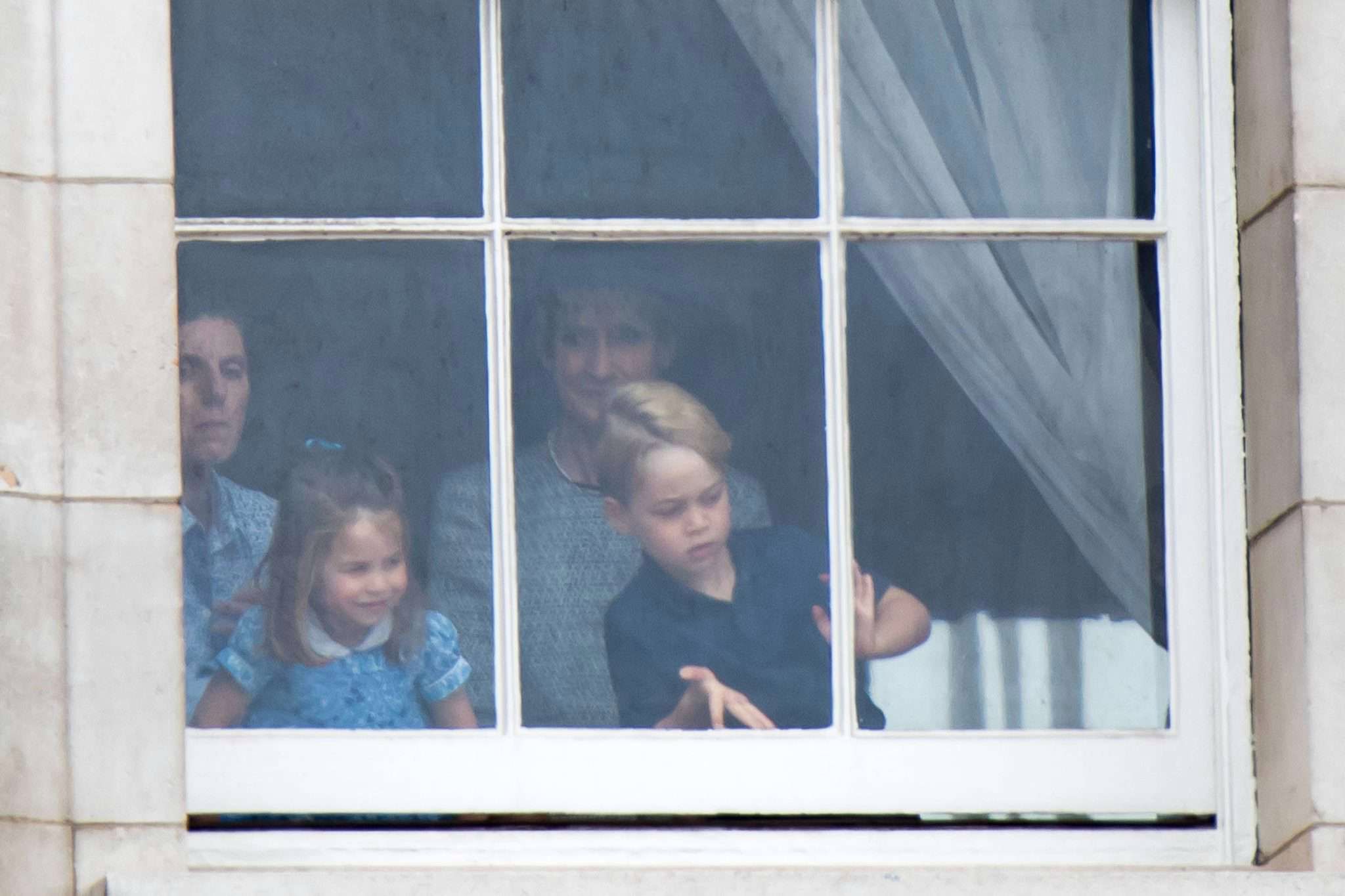 Księżniczka Charlotte i książę George stroją miny w oknie Pałacu Buckingham