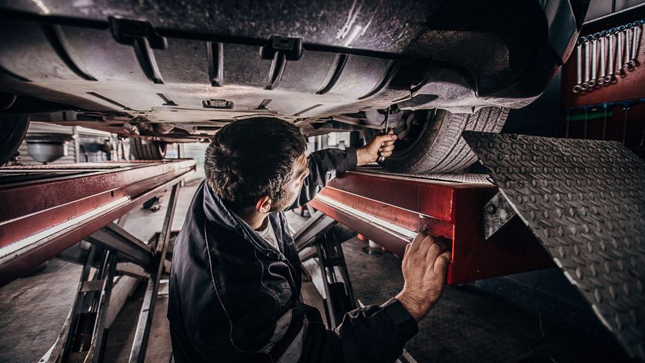 One man, Car mechanic working in auto repair shop, standing beneath the car.