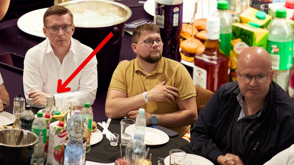 Burmistrz Mateusz Wichert przy stole na gali. Na stole butelka a