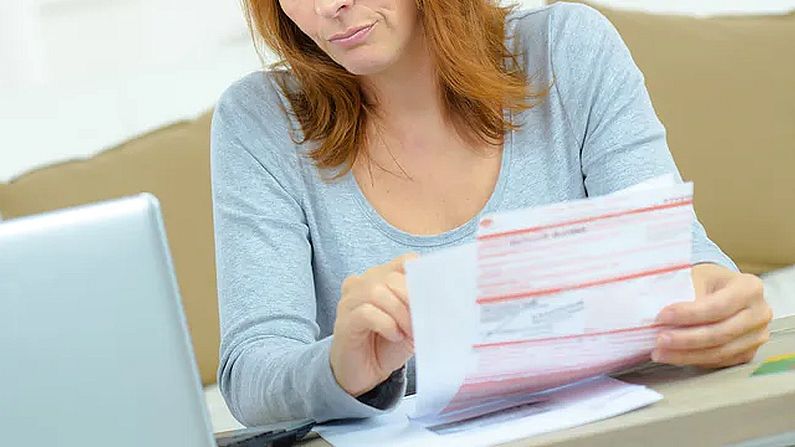 Na zdjęciu kobieta trzymająca w ręku rachunki i wpatrująca się w ekran komputera