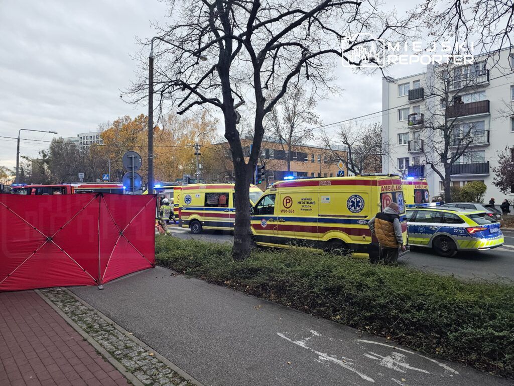 Na ulicy stoją karetki pogotowia oraz radiowóz policji, a w tle widoczny jest czerwony namiot zabezpieczający miejsce zdarzenia.