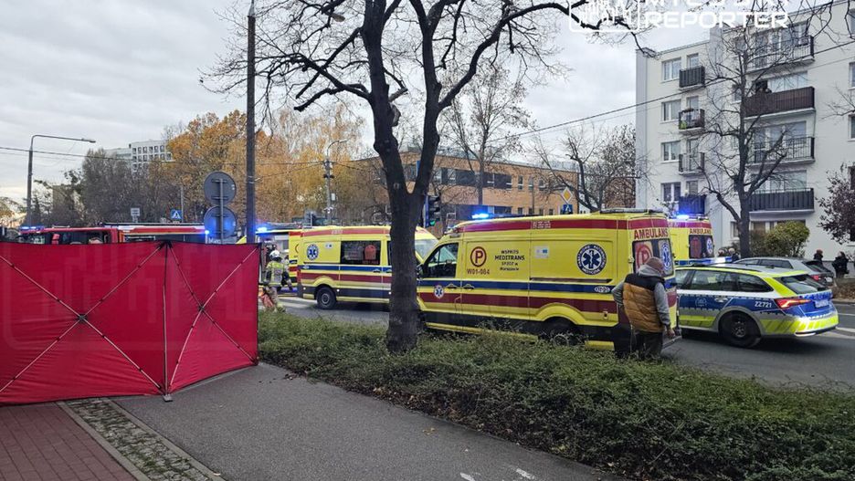 Na ulicy stoją karetki pogotowia oraz radiowóz policji, a w tle widoczny jest czerwony namiot zabezpieczający miejsce zdarzenia.