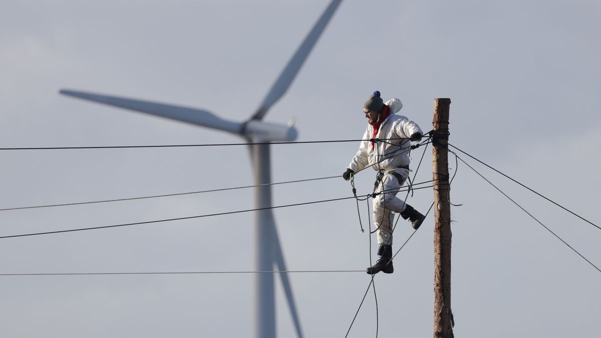 ERKELENZ, GERMANY - JANUARY 11: An activist stands on a rope on a pole as a wind turbine spins behind at the settlement of Luetzerath next to the Garzweiler II open cast coal mine on January 11, 2023 near Erkelenz, Germany. Police are evicting environmental activists who have occupied the abandoned Luetzerath settlement and are seeking to prevent Luetzerath's demolition that will make way for an expansion of the Garzweiler coal mine. The North Rhine-Westphalia state government of German Christian Democrats (CDU) and Greens has approved the demolition and the coal mine expansion, while at the same time announcing an accelerated phase out of coal-fired energy production in the state of North Rhine-Westphalia from 2038 to 2030. Other nearby settlements that were also slated for demolition will now be spared, though critics point out that Germany has sufficient energy production capacity and does not need the coal lying beneath Luetzerath. (Photo by Sean Gallup/Getty Images)