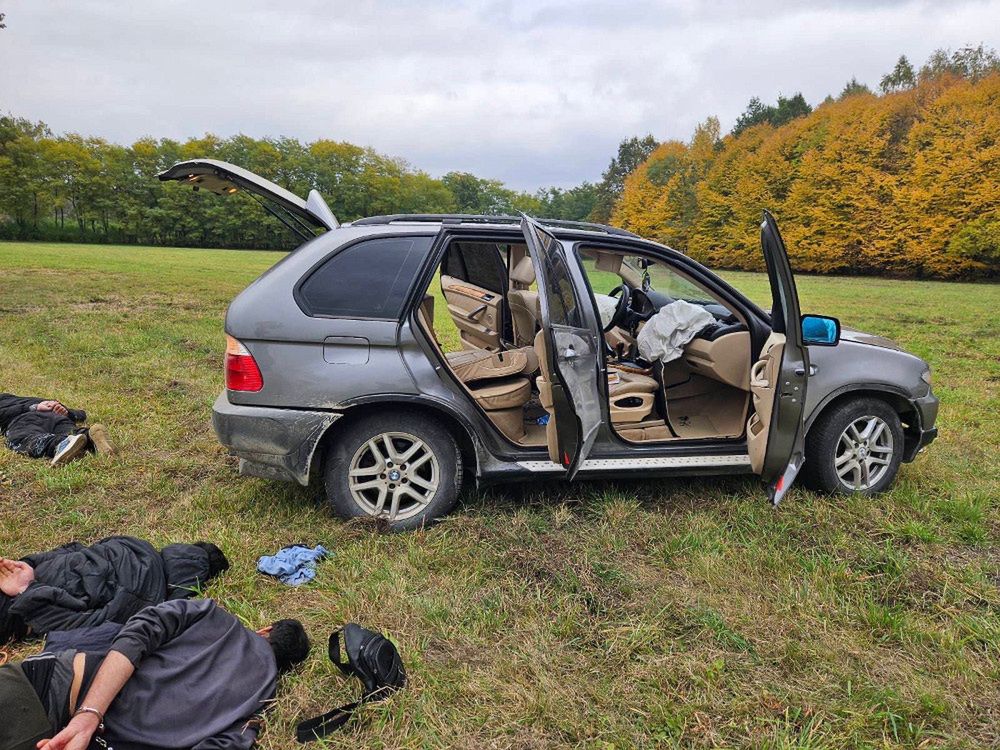 Uszkodzony samochód osobowy stoi na polu, a obok leżą dwie osoby w nieprzytomnym stanie.