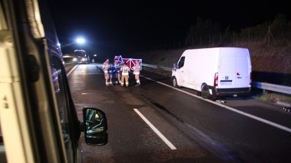 Grupa strażaków udziela pomocy na drodze, obok uszkodzonego białego furgonu w nocy.