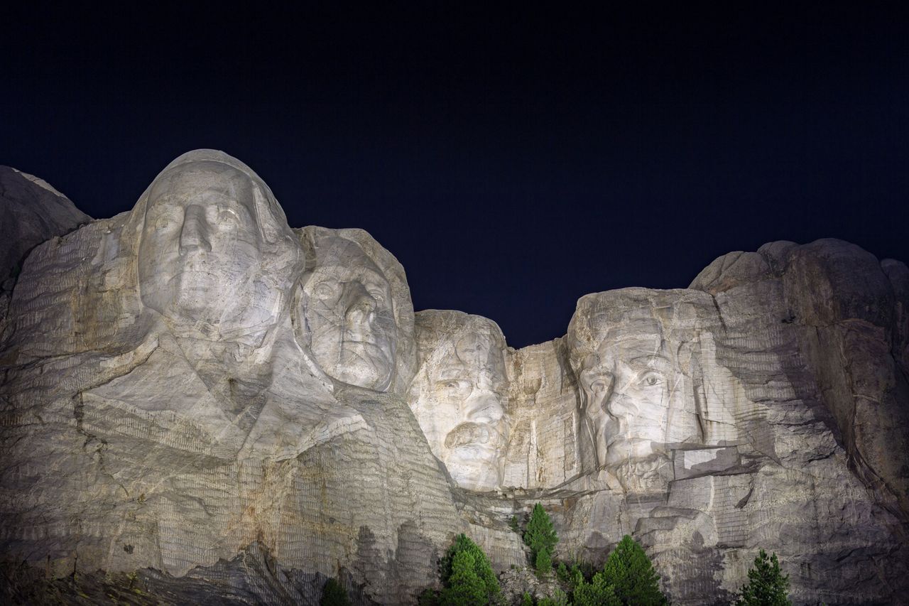 Carved granite busts of George Washington, Thomas Jefferson, Theodore "Teddy" Roosevelt and Abraham Lincoln are framed by trees at Mount Rushmore National Monument near Keystone, South Dakota. (Photo by: Ron Buskirk/UCG/Universal Images Group via Getty Images)