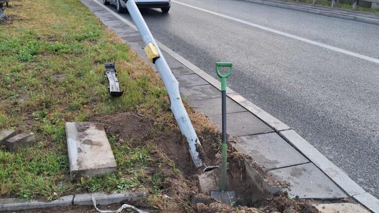 Złamany słup sygnalizacji świetlnej leży obok wykopu przy ulicy, a w tle przejeżdża nieoznakowany radiowóz.