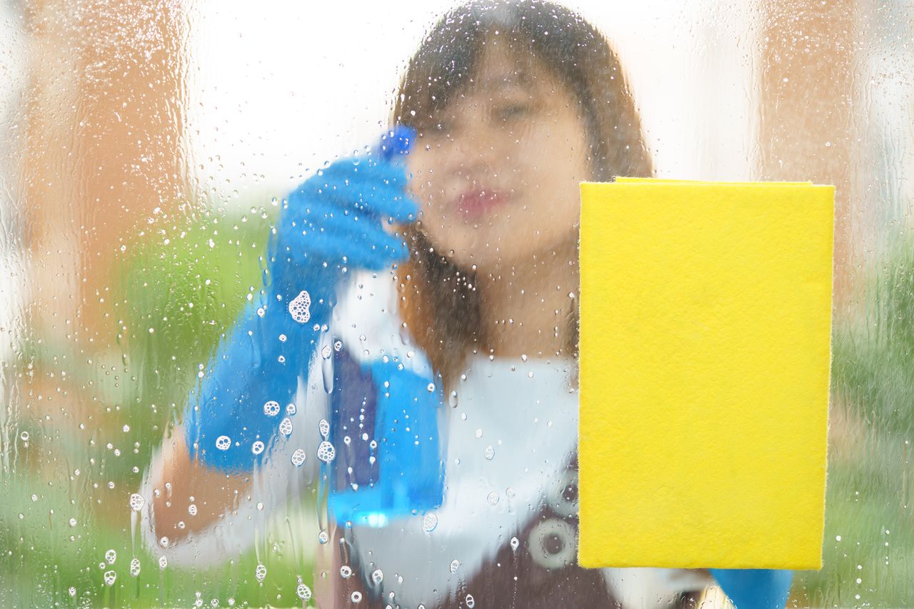 Woman housekeeper cleaning the mirror with yellow sponge