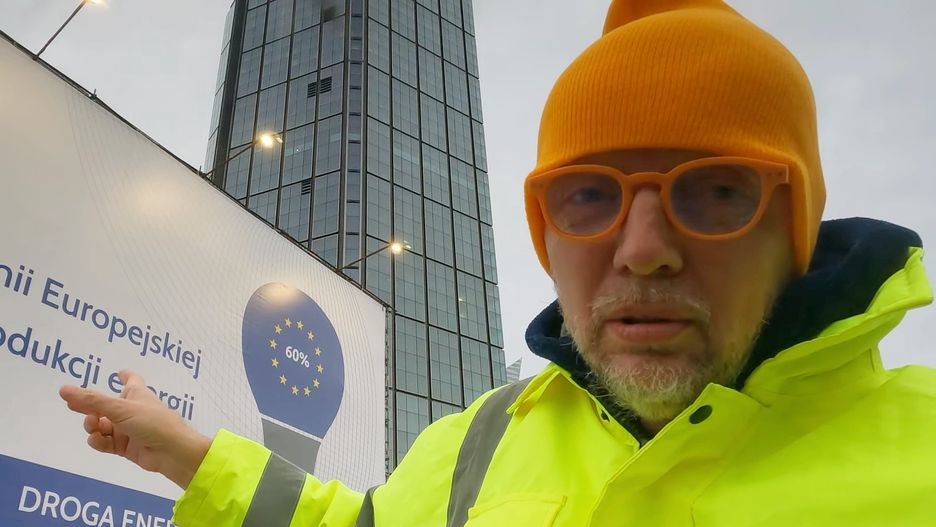 Marcin Mizgalski na tle słynnej kampanii billboardowej o rzekomej drożyźnie spowodowanej przez politykę klimatyczną Unii Europejskiej
