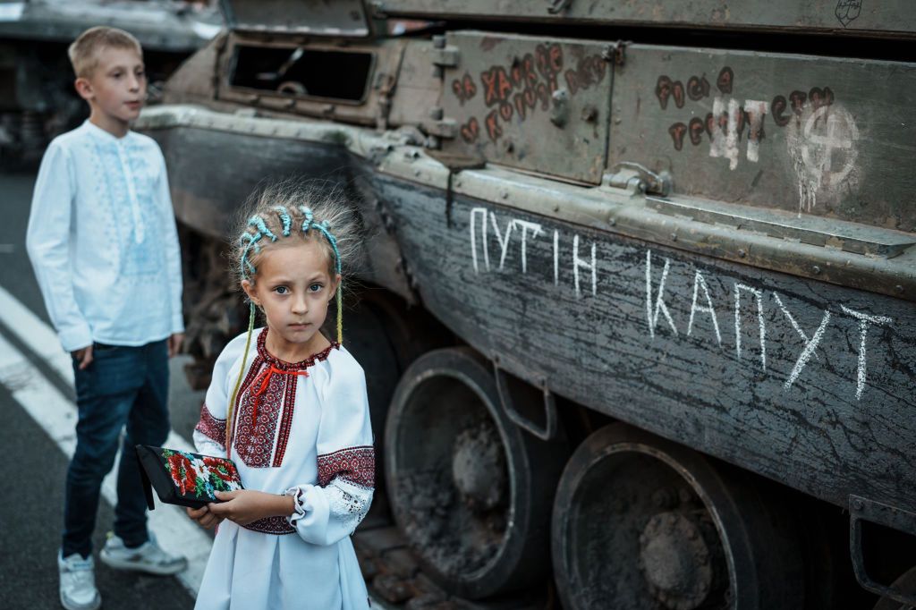 Dziewczynka w Kijowie na tle zniszczonego rosyjskiego czołgu. Napis głosi: Putin kaput!