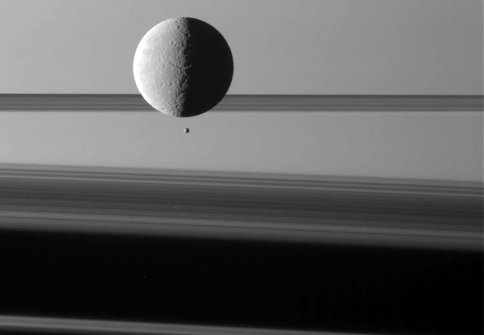 Lodowo-skalista Rea (średnica: 1528 km) oraz mniejszy i nieregularny Epimeteusz (wymiary: 135x108x105 km). W tle Saturn i jego pierścienie. Księżyce te nie są w rzeczywistości blisko siebie. na tym zdjęciu Epimeteusz znajduje się ok. 400 tys. km ze Reą.