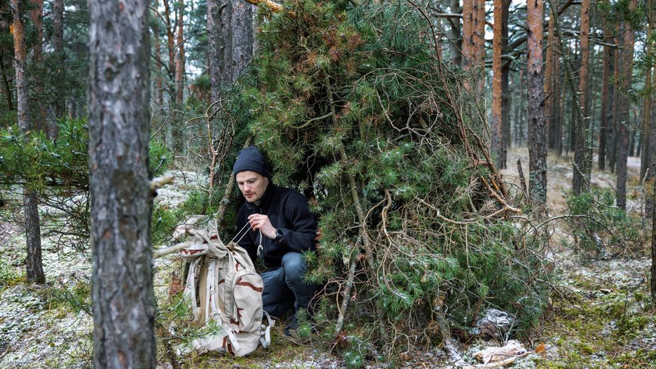 Człowiek w schronie z gałęzi drzewa na łonie natury, survival