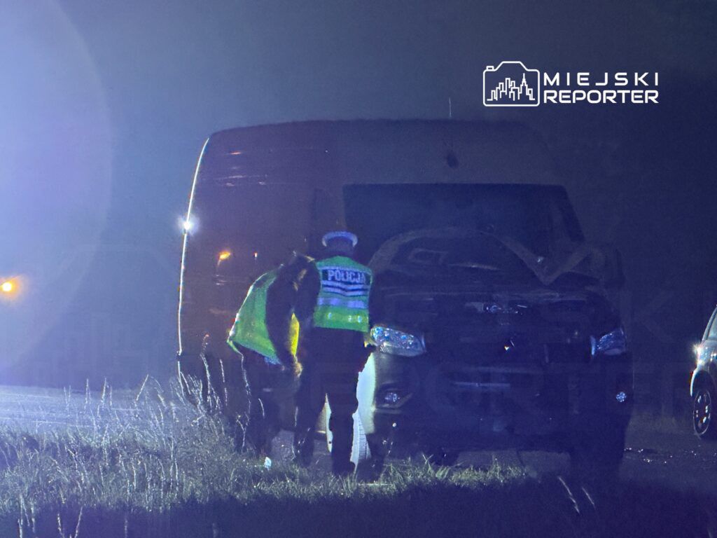 Policjant w kamizelce odblaskowej bada uszkodzony pojazd na poboczu drogi w nocy.