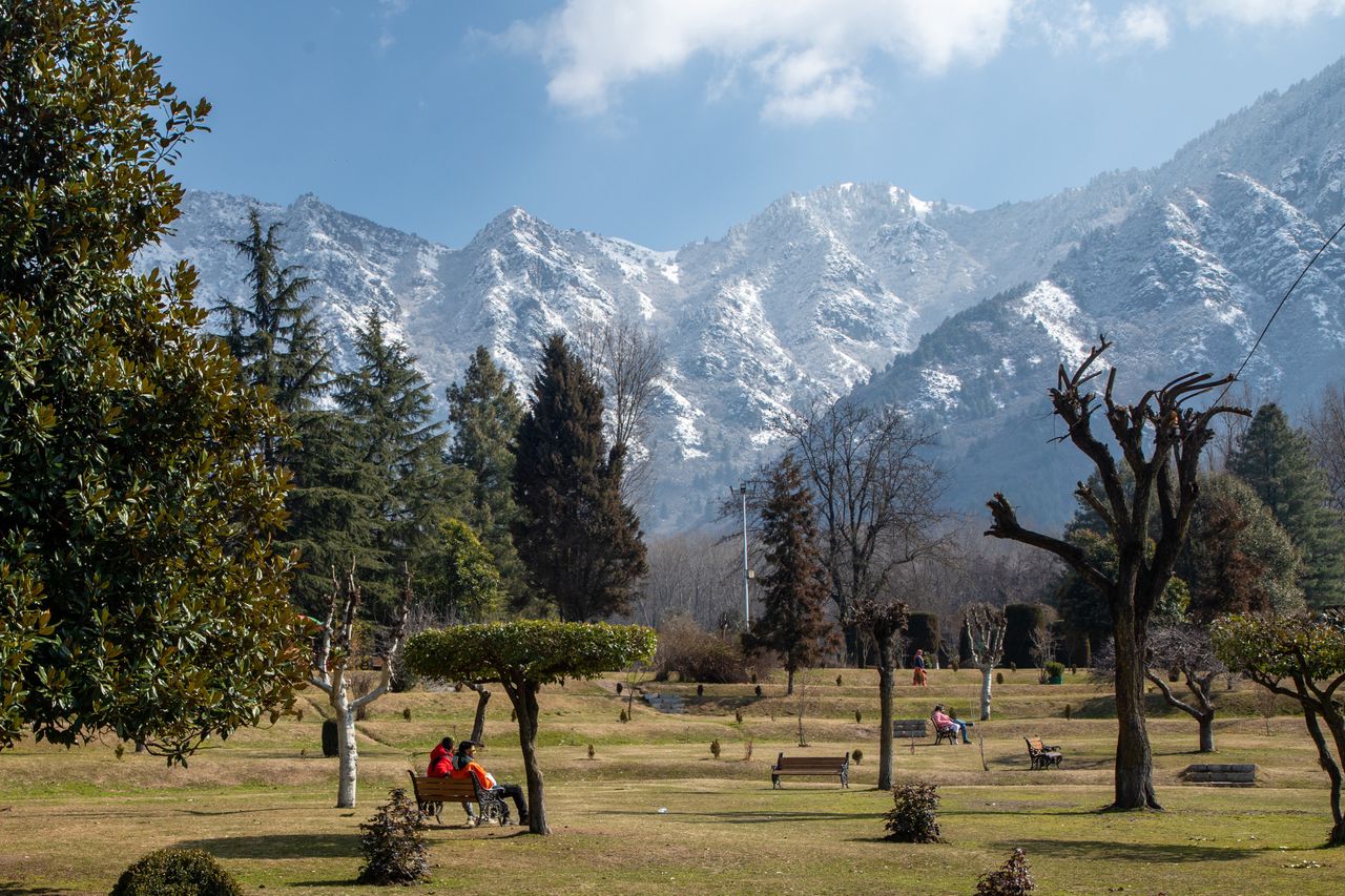 SRINAGAR, JAMMU AND KASHMIR, INDIA - 2024/02/22: Kashmiri people sit on benches inside a garden with a backdrop of snow-covered mountains on a sunny day in Srinagar. The weather improved across Jammu and Kashmir after three days of incessant rain and snowfall. Meanwhile, the daytime temperatures improved with bright sunshine witnessed in many parts of the valley, including the summer capital Srinagar. The Dal Lake, apart from being the prime tourist attraction, is also home to over sixty thousand people, whose primary source of income comes from tourism and agriculture. (Photo by Faisal Bashir/SOPA Images/LightRocket via Getty Images)