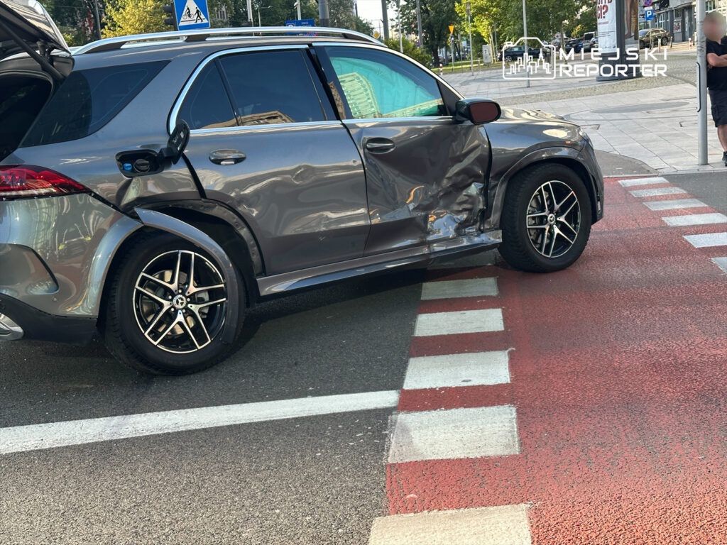 Uszkodzony samochód osobowy zaparkowany na przejściu dla pieszych, z widocznymi zarysowaniami na karoserii.