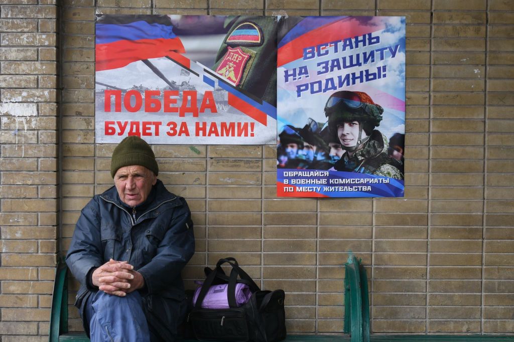 Mieszkaniec Doniecka siedzi pod plakatami propagandowymi armii prorosyjskiej
