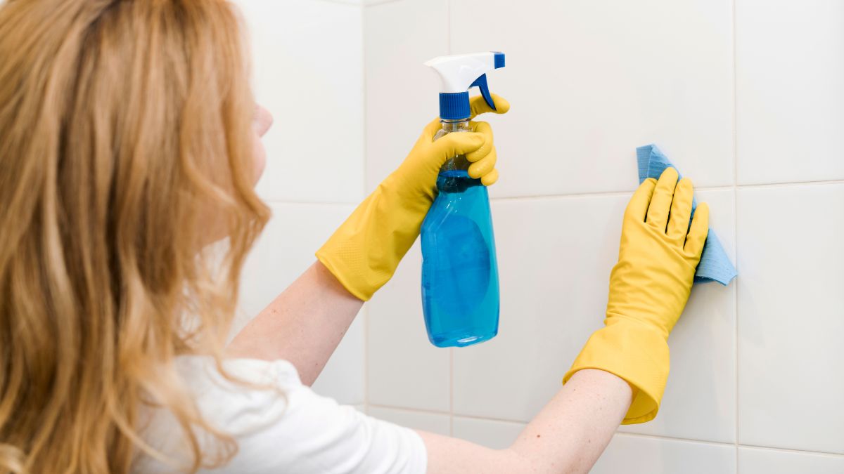 Kobieta czyści kafle łazienkowe.