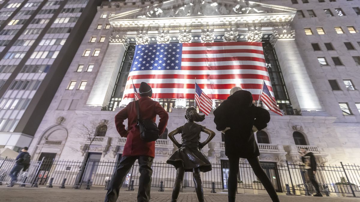 The Fearless Girl bronze sculpture by Kristen Visbal, stands across the New York Stock Exchange building and people are passing by. Night view of the illuminated exterior of New York Stock Exchange with a big American flag from the front facade. NYSE building has the style of classical architecture of Greece with columns, the inscription New York Stock Exchange and US flags hanging. The financial organization at Wall Street is a symbol for the global and American Economy as one of the most powerful financial institution located in Wall Street at lower Manhattan in New York City, United States of America. The US stock market is reacting with heavy losses after president Trump tariffs announcement on April 2025. November 2024 in NYC, USA  (Photo by Nicolas Economou/NurPhoto via Getty Images)